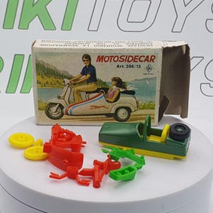 Könnte beinhalten: Ein Vintage-Spielzeugset mit einem grünen und gelben Beiwagen, unmontierten roten und gelben Teilen und einer Box mit der Aufschrift "MOTOSIDECAR". Die Box zeigt eine Illustration eines Rollers mit Beiwagen.