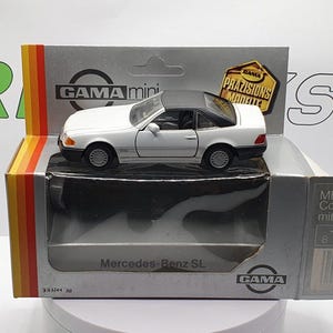 Può includere: Modello di auto Mercedes-Benz SL Coupé bianco con tetto nero e ruote nere. L'auto è su una base di esposizione bianca con il testo "Mercedes-Benz SL" e "GAMA" stampato su di essa. La scatola è bianca con strisce rosse, gialle e blu. Il testo "GAMA mini" e "DAMA PRÄZISIONS MODELLE" è stampato sulla scatola.