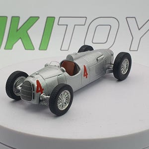 Può includere: Modello di auto da corsa vintage argentata con il numero 4 in rosso sul lato. L'auto ha pneumatici neri e interni marroni. Il modello è su una superficie bianca.