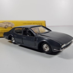 May include: A dark gray toy car model with a black interior and chrome wheels. The car is a sedan with a long hood and a short trunk. The car is sitting on a white surface.