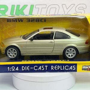 May include: A gold-colored BMW 328Ci die-cast replica car in a display box. The box is yellow and blue with the text "BMW 328Ci" and "1:24 Die-Cast Replicas". The car has a sunroof and detailed wheels.