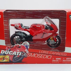 Może przedstawiać: Czerwony model motocykla Ducati Desmosedici w pudełku. Model w skali 1:18 z numerem 65. Pudełko z logo Ducati Corse i nazwiskiem Loris Capirossi.