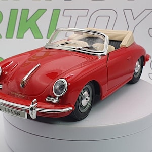May include: A red toy convertible car with a tan roof. The model car has a silver front bumper and headlights. The license plate reads "S-DA 534". The car is on a white surface.