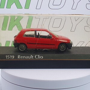 Può includere: Un'auto modello Renault Clio rossa in una vetrina trasparente. Il modello è su una base nera con la scritta "1519 Renault Clio". L'auto ha ruote e finiture nere. La vetrina è su una superficie bianca.
