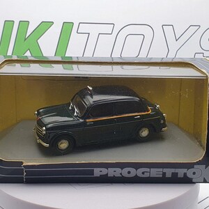 Peut inclure: Un modèle de voiture jouet vert dans une boîte d'exposition. La voiture a un signe de taxi jaune sur le dessus et est posée sur un fond jaune. La boîte porte l'inscription "ProgettoK".