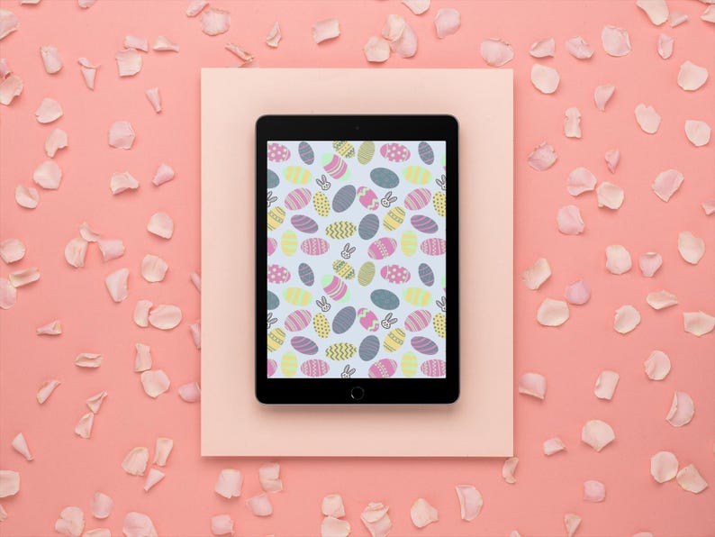 May include: A black tablet shows a colourful Easter egg pattern on a light blue background. The tablet is on a light pink rectangle, surrounded by a pink background and scattered flower petals. The egg design includes various colours and patterns.