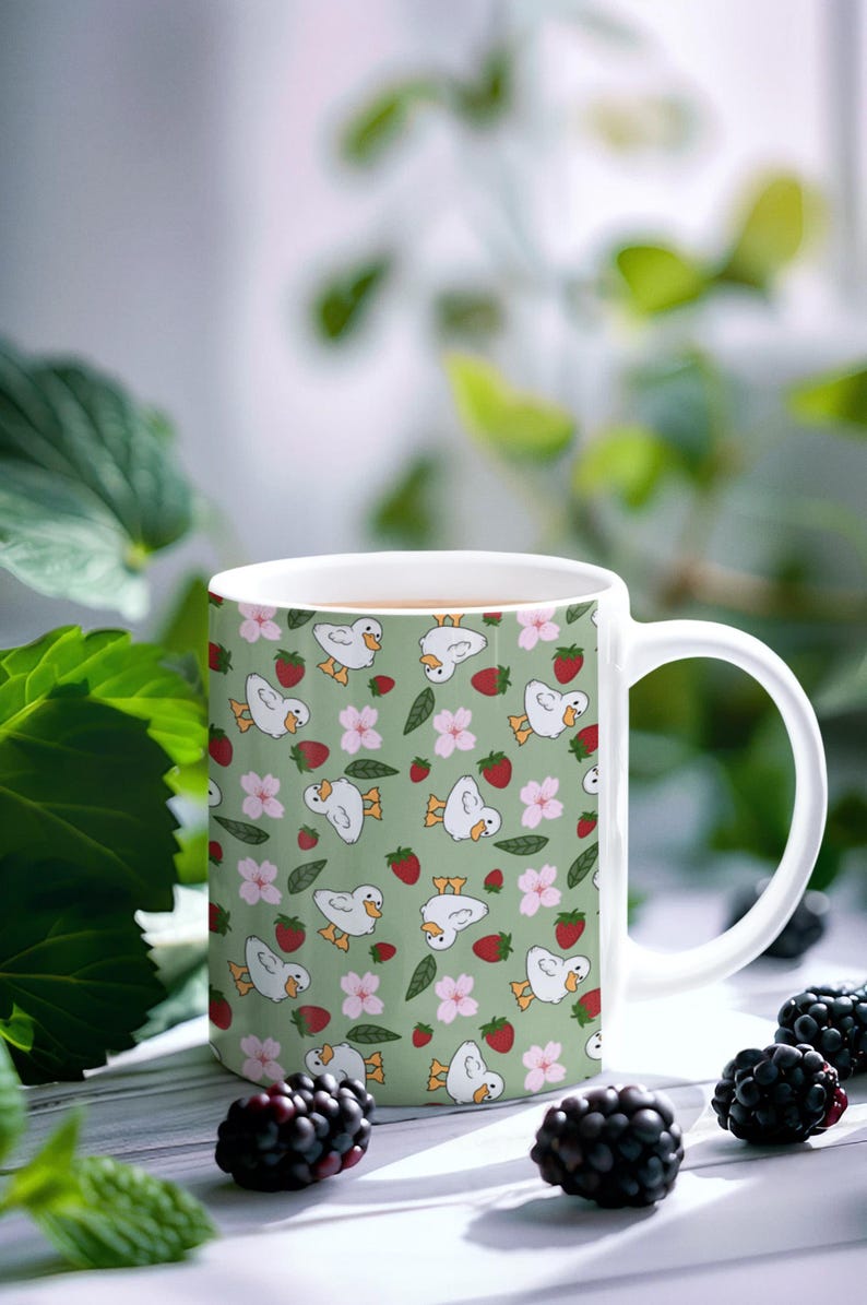 Puede incluir: Taza de cer&aacute;mica blanca con un patr&oacute;n repetido de patos de dibujos animados, fresas y flores rosas sobre un fondo verde claro. La taza tiene un asa curva y est&aacute; llena de un l&iacute;quido marr&oacute;n claro. Un producto de cocina y comedor.