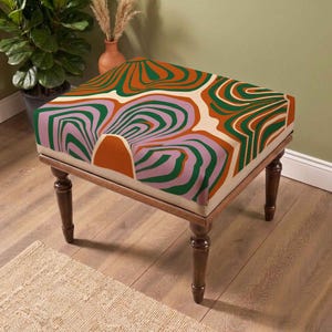 May include: A square ottoman featuring a cream-colored fabric top with a repeating abstract pattern of wavy, concentric lines in shades of burnt orange, forest green, and lavender. The piece is supported by four dark brown, turned wooden legs.