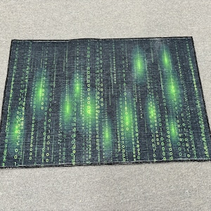 May include: A black and green rug with a digital pattern of ones and zeros. The rug has a fringe border.