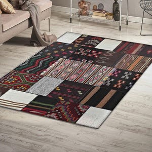 Peut inclure: Tapis rectangulaire en patchwork avec des motifs géométriques et tribaux noirs, rouges, blancs et bruns. Le tapis est posé sur un parquet clair dans un salon. Les dimensions du tapis sont en centimètres.