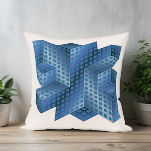 Op de afbeelding: Een vierkant kussen met een geometrisch ontwerp in tinten blauw, turquoise en paars. Het ontwerp lijkt op een 3D-kubus of structuur, met een rasterpatroon. Het kussen ligt op een houten oppervlak.