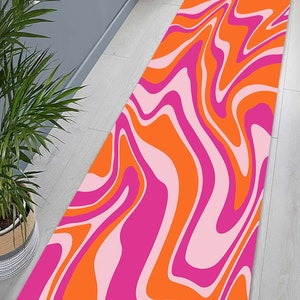 Op de afbeelding: Een lang, rechthoekig tapijt met een abstract swirl-patroon in roze en oranje. Het tapijt heeft een modern, eigentijds ontwerp.