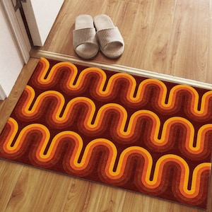 Könnte beinhalten: Eine braune Fußmatte mit einem wellenförmigen Muster in Orange- und Gelbtönen. Das Muster ähnelt einer Reihe sich überlappender Bögen.