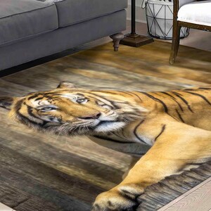 May include: A brown and black tiger rug with a wood grain background. The tiger is lying on its side with its head resting on the floor. The rug is perfect for adding a touch of wildness to any room.