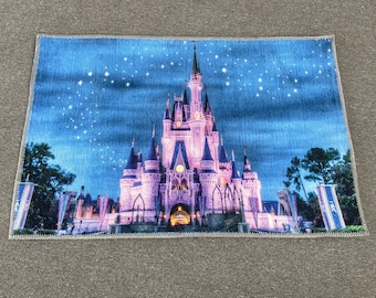 May include: A pink and white castle with blue and white stars in the background. The castle is lit up at night and has a blue sky behind it.