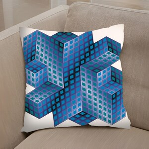 Op de afbeelding: Vierkant kussen met een geometrisch ontwerp. Het kussen heeft een herhalend patroon van blauwe en teal kubussen op een witte achtergrond. De kubussen hebben een driedimensionale uitstraling, waardoor een optische illusie ontstaat. Het kussen is vierkant en lijkt gemaakt van een zachte stof.
