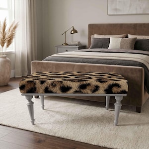 Puede incluir: Un banco rectangular con un asiento tapizado en estampado de leopardo marrón y negro. El banco se apoya sobre cuatro patas de madera torneada de color gris claro que se estrechan hacia la parte inferior, ofreciendo una base estable.