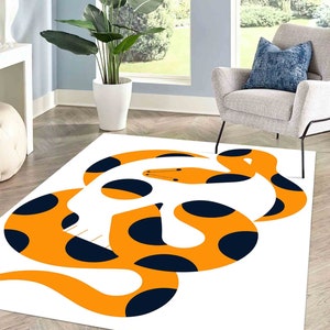 May include: A white rug featuring a large orange and black snake design. The snake is curled up in a circle and has black polka dots.