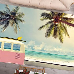 May include: A pink vintage van with a surfboard on top parked on a beach with palm trees and a blue ocean in the background.