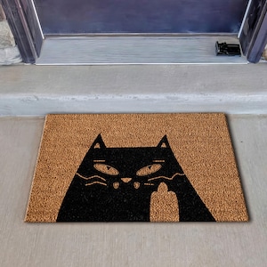 May include: A brown coir doormat with a black silhouette of a cat giving the middle finger.