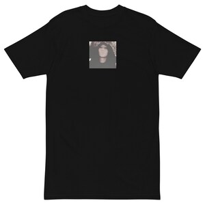 May include: Black t-shirt with a square image of a person with long dark hair.