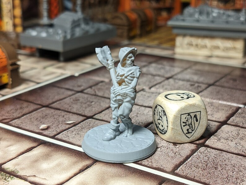 May include: A gray plastic miniature skeleton figure holding a weapon, standing on a gray base. A wooden dice with a skull and shield design is in the background.