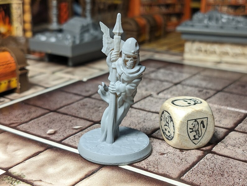 May include: A gray plastic miniature of a skeletal figure wearing a hooded robe and holding a spear. The figure is standing on a round base. A wooden dice with a skull and a coat of arms is in the background.