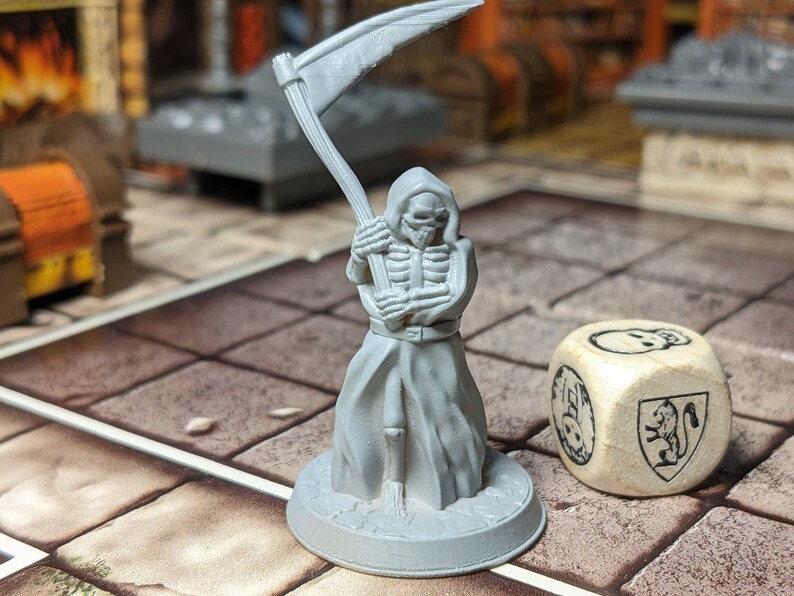 May include: A gray plastic miniature of a skeletal figure in a hooded robe, holding a scythe. The figure is standing on a round base. A wooden dice with a skull and a lion symbol is in the foreground.