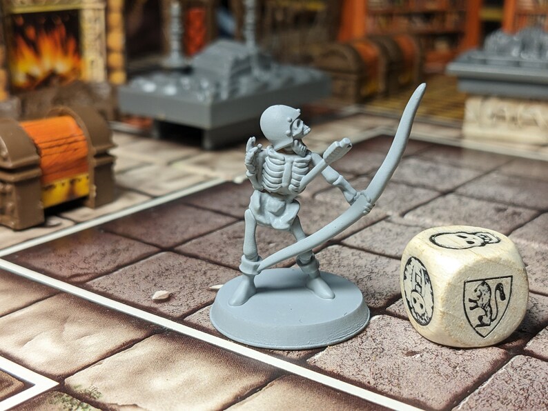 May include: A gray plastic miniature skeleton archer figure holding a bow and arrow, standing on a gray base. The figure is posed as if it is aiming the bow and arrow. A white wooden dice with a skull and a squirrel design is in the background.
