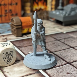 May include: A gray plastic miniature figure of a skeletal warrior holding a spear. The figure is standing on a round base. A wooden dice with a skull and a lion crest is in the foreground.