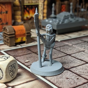 May include: A gray plastic miniature skeleton figure holding a spear, standing on a gray base. The figure is on a brown and white tiled surface.