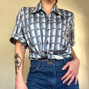 May include: A blue and white plaid button-up shirt with short sleeves, tied at the waist. The shirt is worn with denim shorts.