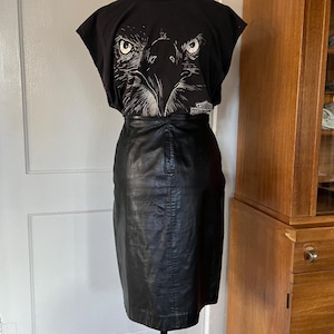 May include: A black leather skirt with a zipper closure and a black t-shirt with a white eagle graphic and the text "Harley Davidson" on the bottom.