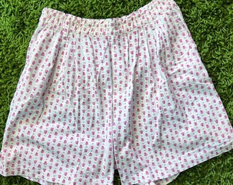 May include: White shorts with an elasticated waistband, patterned with small pink floral motifs. The shorts are made of a lightweight fabric, suitable for warmer weather.