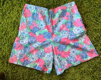 May include: Shorts with a colourful floral print. The shorts display a pattern of pink, blue, and green flowers on a light blue backdrop. They have an elasticated waistband and are made from a lightweight material. The shorts are ideal for summer.