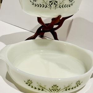 May include: Two white ceramic baking dishes with green floral designs. The dishes are stacked on a wooden stand.