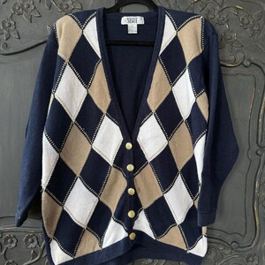 May include: Navy blue argyle cardigan sweater with gold buttons. The sweater features a V-neck and long sleeves. The argyle pattern includes navy, white, and tan diamonds. The label reads "SEGLE".