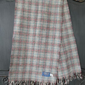 May include: A multi-colored plaid scarf with a fringed edge. The scarf features a pattern of red, blue, green, and black squares on a cream background. A small blue tag is attached to the scarf.