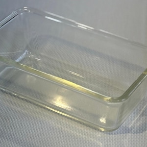 May include: A clear, rectangular glass baking dish. The dish has a simple, classic design with slightly rounded corners and a smooth surface. It is ideal for baking and serving various dishes.