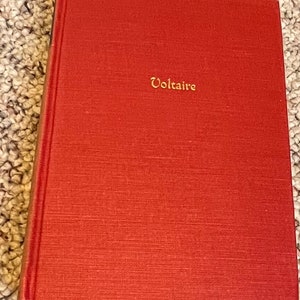 May include: A red hardcover book with the word "Voltaire" in gold lettering on the front cover.
