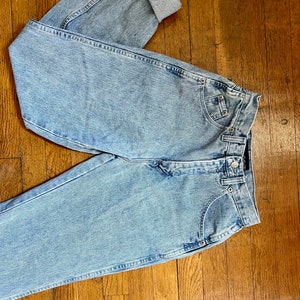 May include: Light blue denim jeans with a high waist and cuffed legs. The jeans have a faded look and are made of a soft, comfortable material.