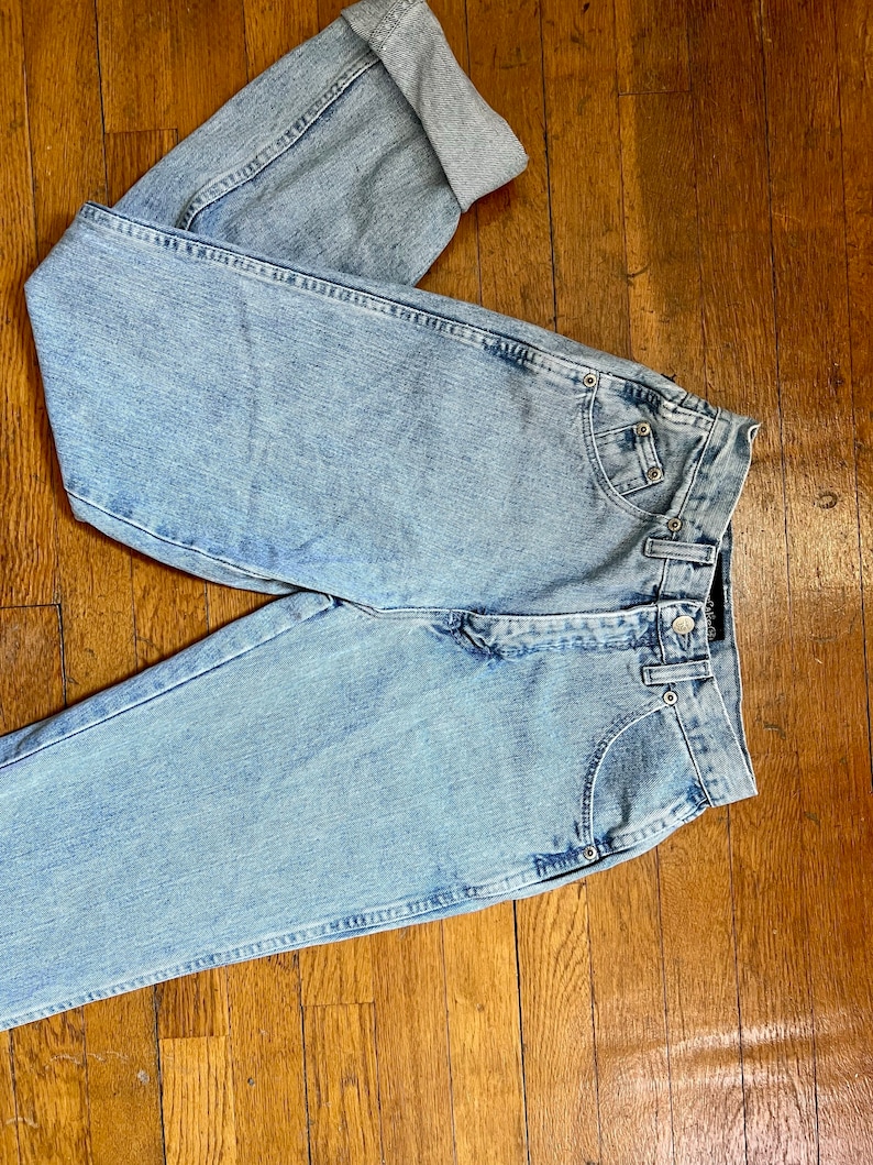 May include: Light blue denim jeans with a high waist and cuffed legs. The jeans have a faded look and are made of a soft, comfortable material.