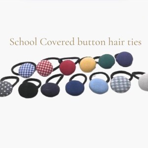 May include: A set of 12 school-themed hair ties with covered buttons. The buttons are in various colours and patterns, including red gingham, blue gingham, white polka dots, black, navy blue, light blue, yellow, green, and grey.