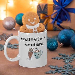 May include: White ceramic mug with a gingerbread man on top. The mug has a design of a milkshake and a cup of hot chocolate with the text "Sweet Treats with Paw and Meme".