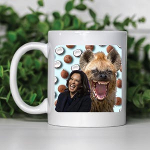 May include: White ceramic mug with a colorful design featuring a laughing hyena and a woman with a bright smile. The background is a light blue with a pattern of coconuts.