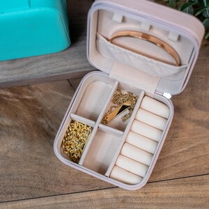 May include: A light pink jewelry box with a velvet interior. The box has multiple compartments for storing rings, necklaces, and earrings. The box is open and the compartments are empty.