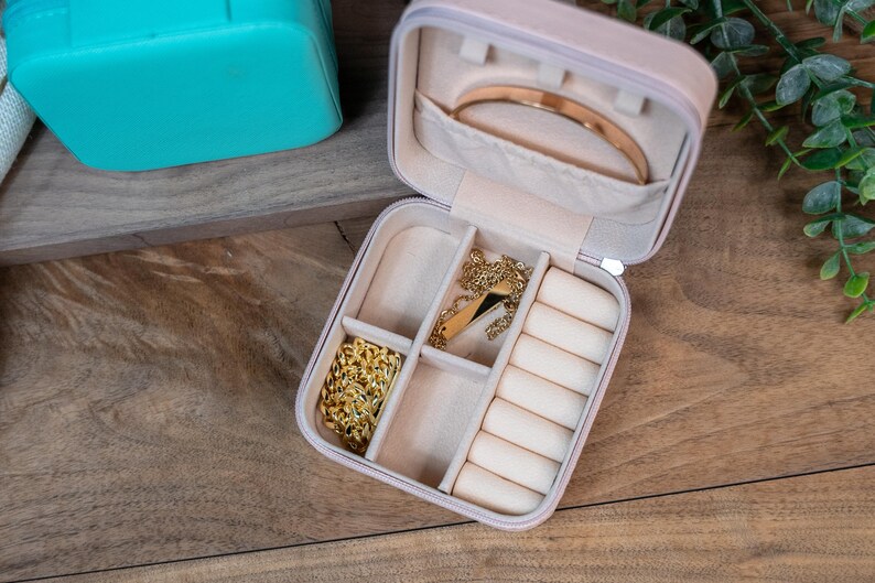 May include: A light pink jewelry box with a velvet interior. The box has multiple compartments for storing rings, necklaces, and earrings. The box is open and the compartments are empty.