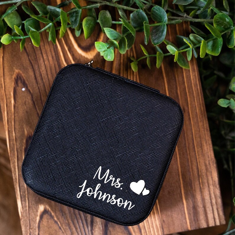 May include: Black jewelry box with a zipper closure. The box has the text "Mrs. Johnson" and two white hearts printed on the front.