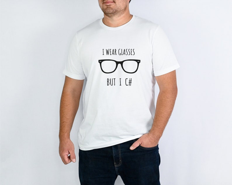 Puede incluir: Camiseta blanca con el texto negro "I wear glasses but I C#" y un dise&ntilde;o de gafas negras. Prenda de vestir informal.