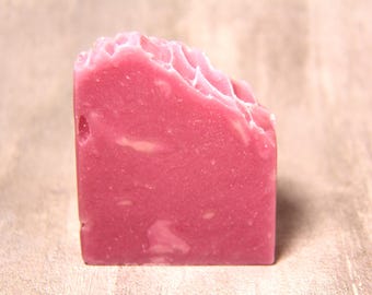May include: A rectangular bar of solid pink soap with a smooth, flat front surface and a textured, wavy top edge. The soap features subtle variations in color with lighter pink swirls throughout the dense, opaque, and matte-finished material.